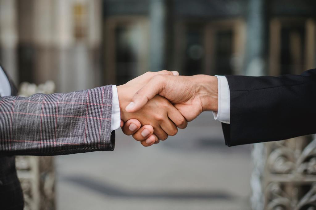 Close-up of two light-skinned people in suits shaking hands