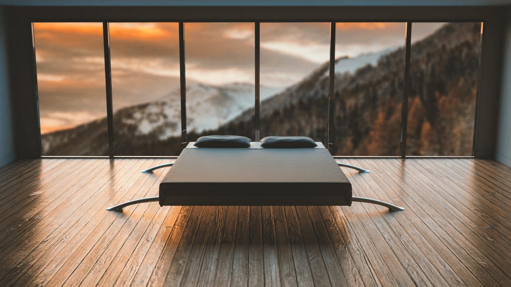 Digital rendering of a minimalist double bed on a wooden plank floor. Floor-to-ceiling windows overlook a mountainscape